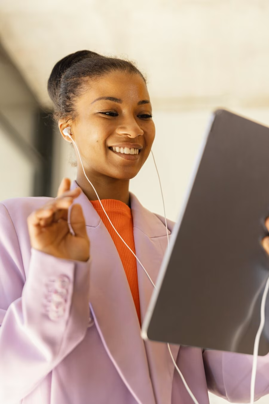 A woman in a lilac blazer works on a tablet during an online meeting