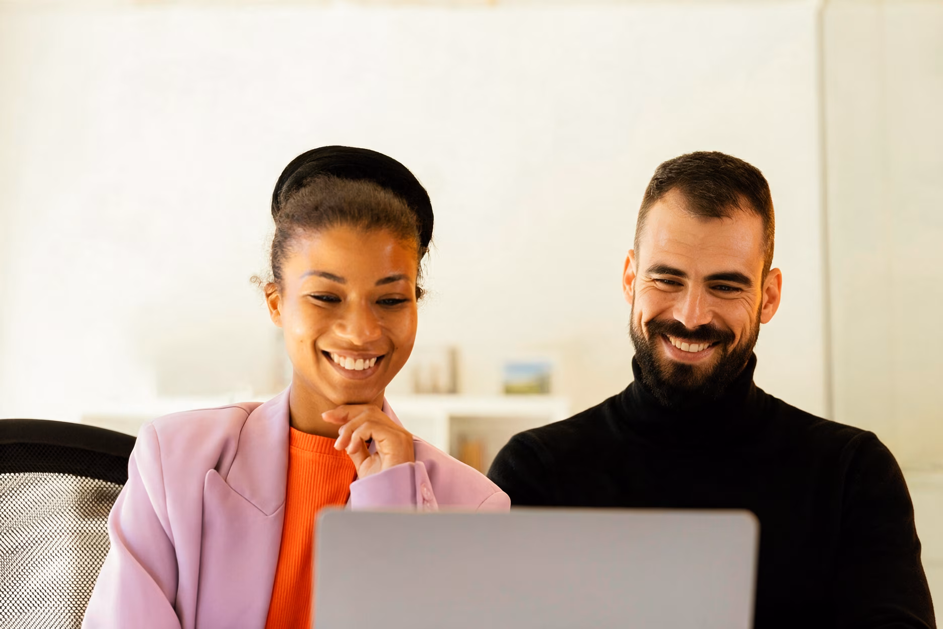 The same woman and her colleague smile as they work together at a laptop